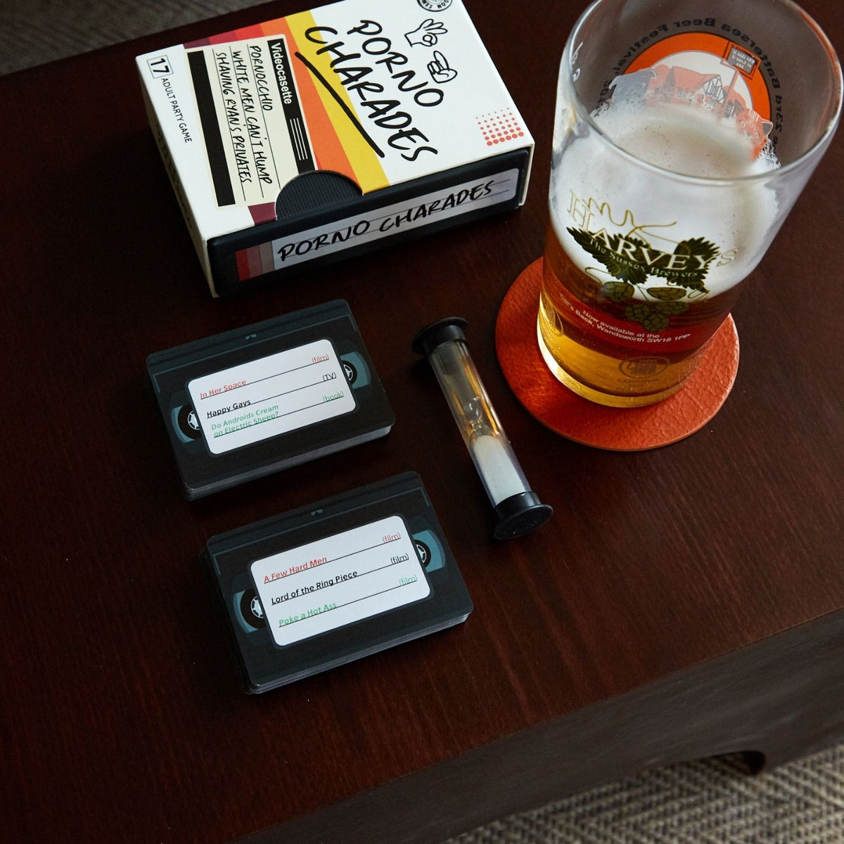 Pornographic movie box, VHS tapes, and a glass of beer on a wooden table.