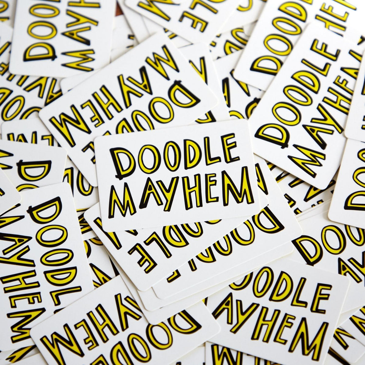The image shows the box of the &#39;Doodle Mayhem&#39; bankers drawing game. It features a white background with doodle-style illustrations of various objects and characters, such as a clock, a shoe, and a musical instrument, in a colorful and playful design.