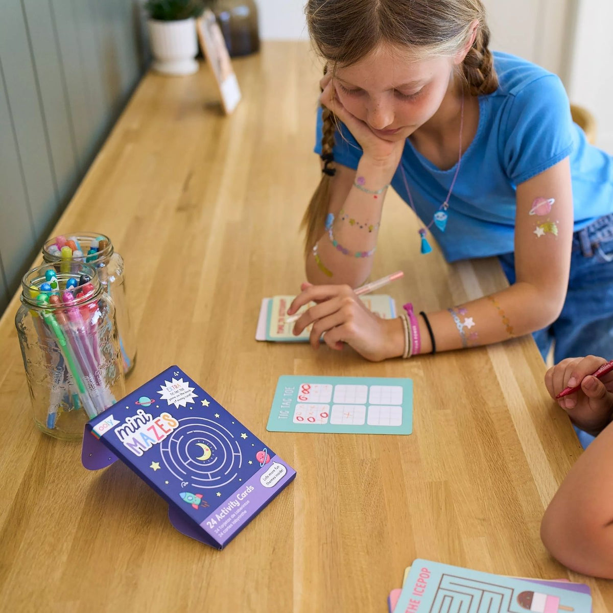 two kids drawing in the Mini Mazes Activity Cards featuring space-themed illustrations with rockets and planets, 