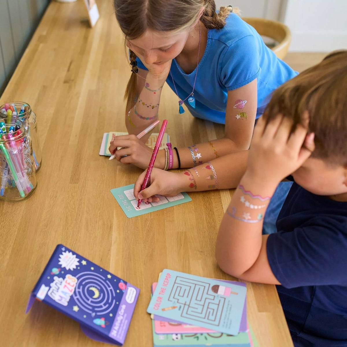 two kids drawing in the Mini Mazes Activity Cards featuring space-themed illustrations with rockets and planets, 