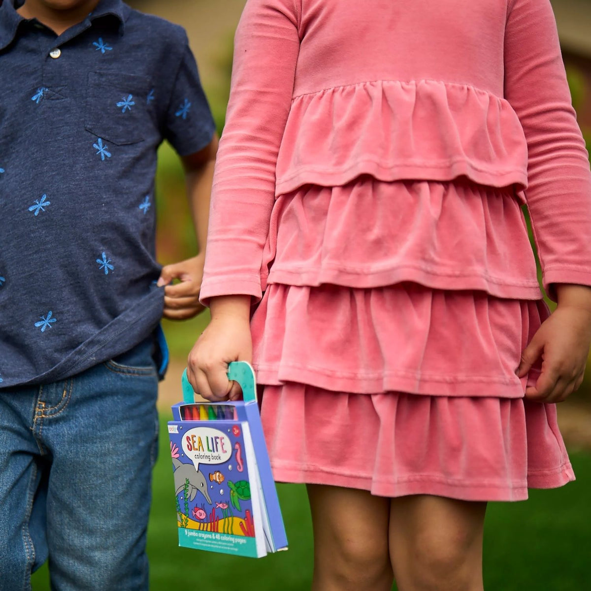 a girl and boy in garden carrying Carry Along Crayon Book each