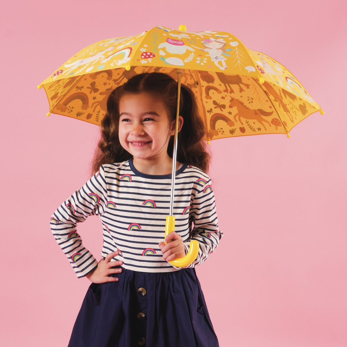 A colorful children&#39;s umbrella with a pattern of unicorns, rainbows, fairies, and llamas. The umbrella is shown both open and closed, with a yellow handle and multicolored panels.