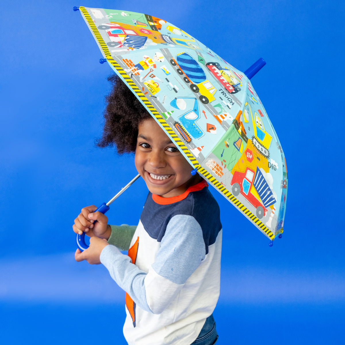 a boy holding A children&#39;s umbrella with a construction theme, featuring illustrations of builders, trucks, and diggers. It is designed to change color when it rains.