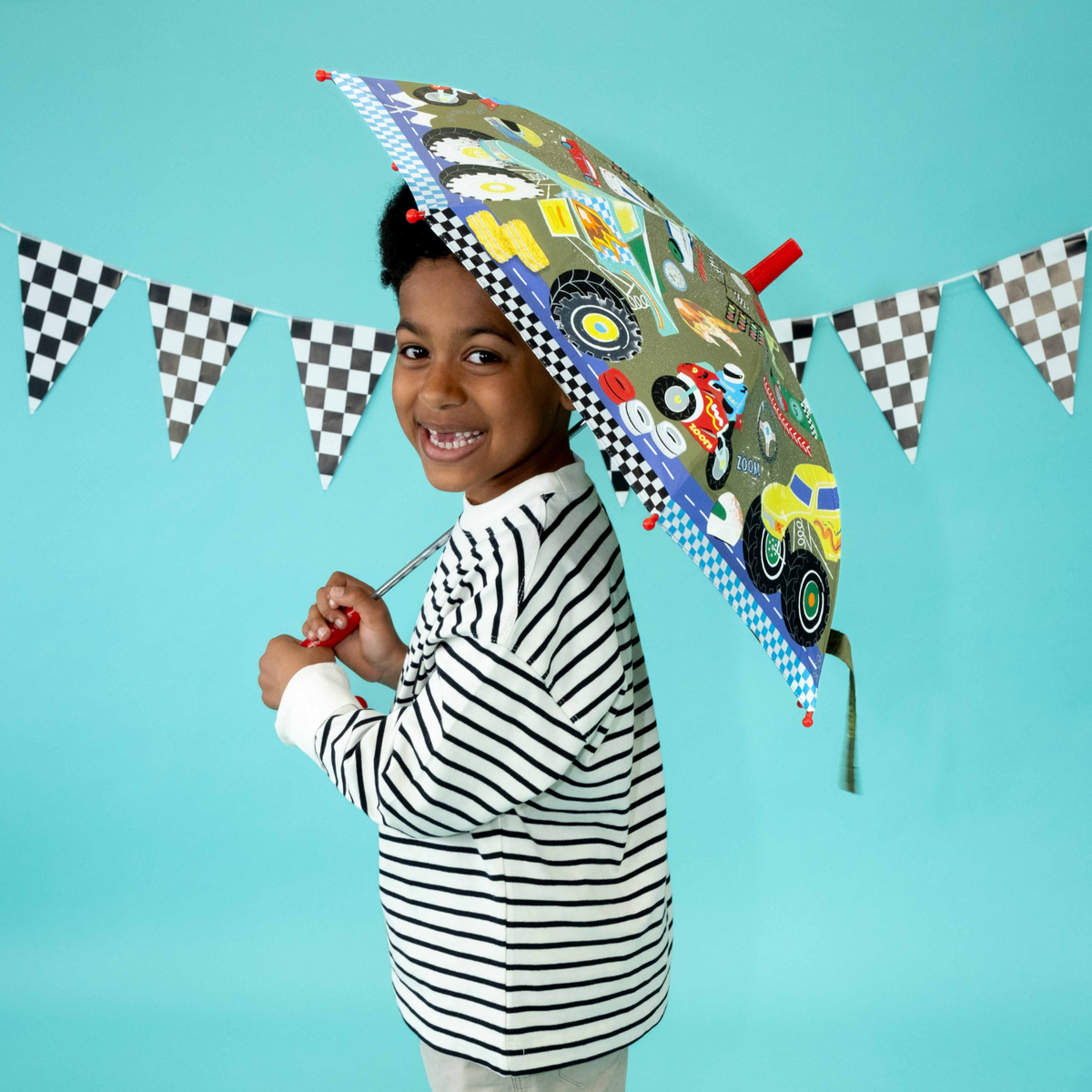 a boy holding A color changing umbrella with a pattern of cars, motorbikes, and monster trucks in vibrant colors.