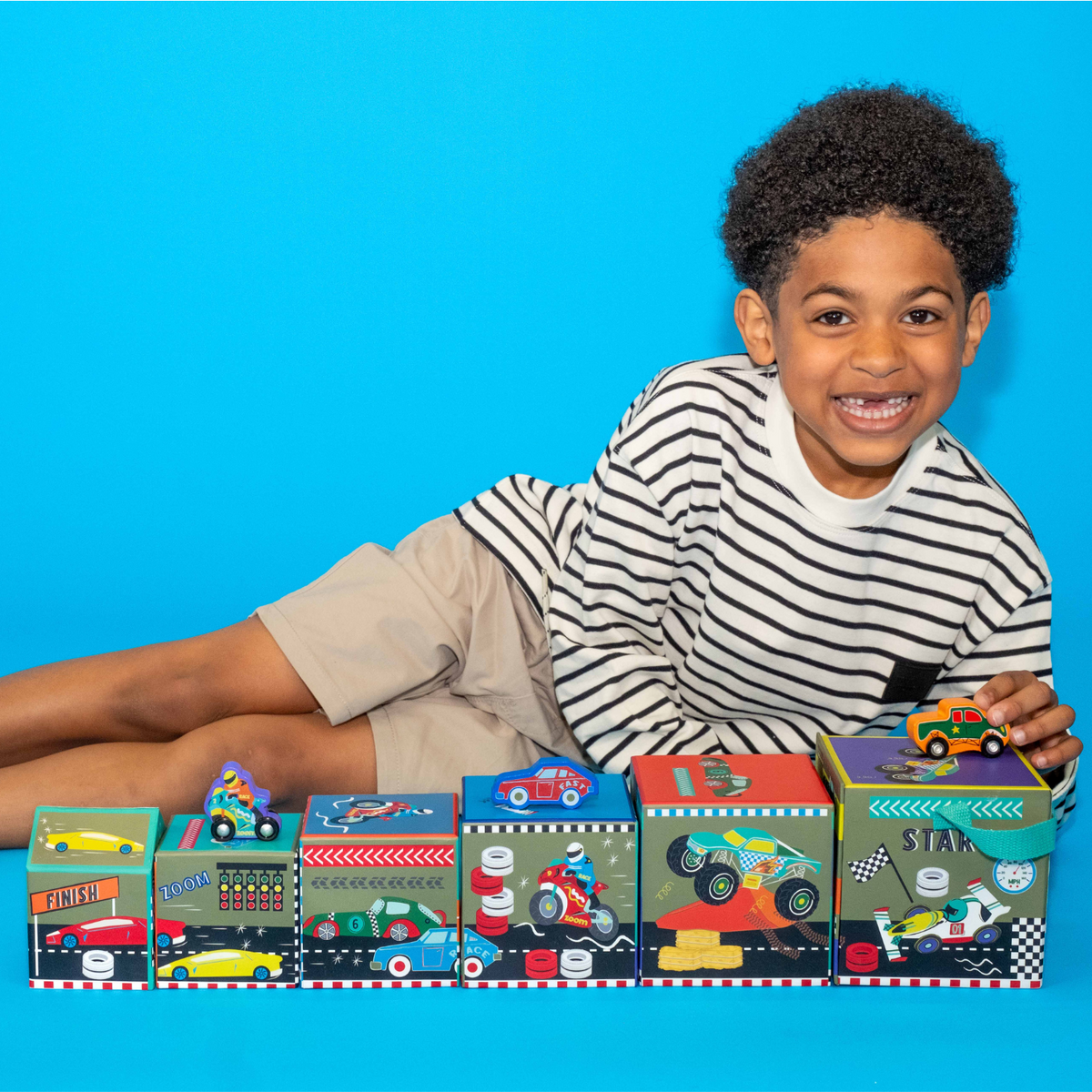 a boy lying down next to the cars stack and play