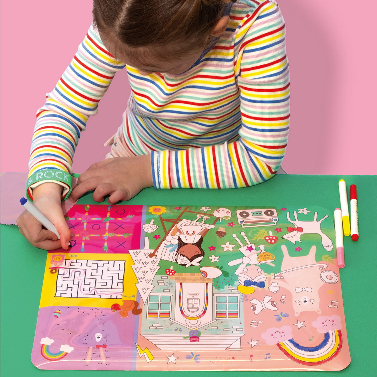 a girl sitting at a table colouring in the rainbow fairy mat