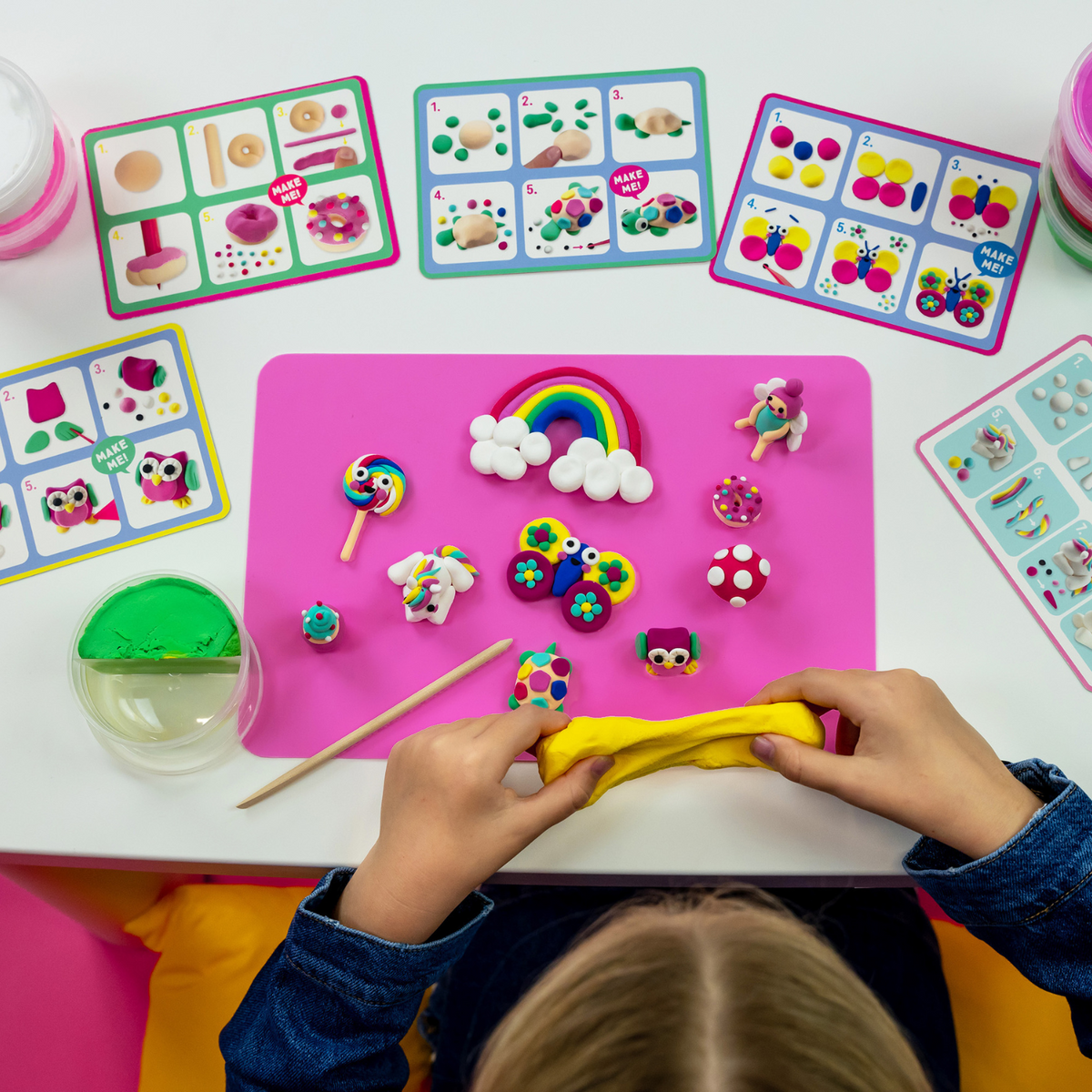 a girl sitting at a table playing with the rainbow fairy clay and play