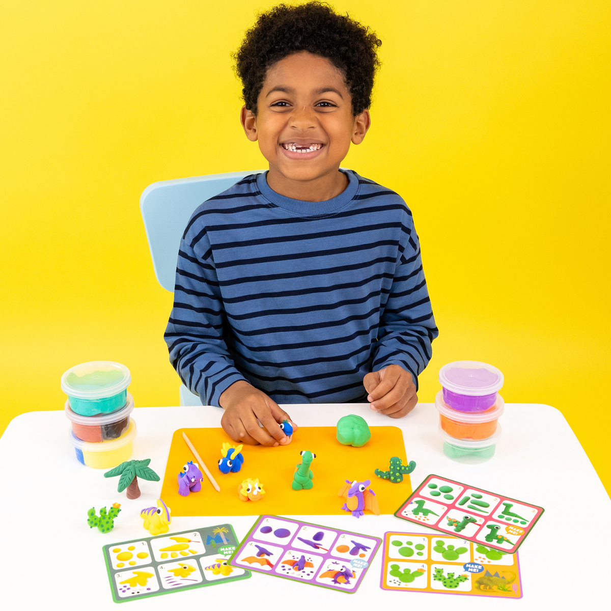 a boy sitting at a table playing with the dinosaur clay and play