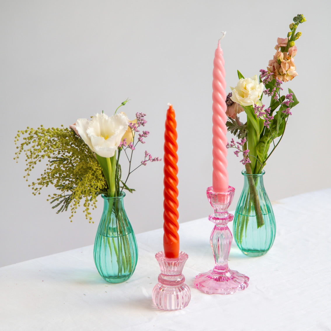 orange and pink Coloured Spiral Candles in pink glass holders on a table 