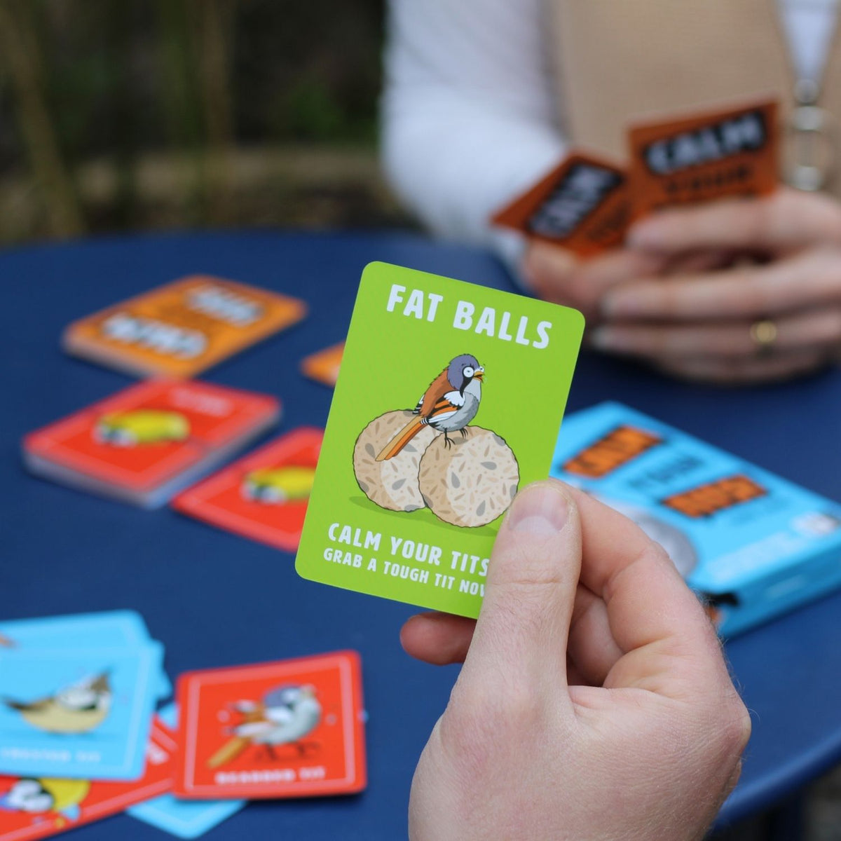 The image shows a box of the &#39;Calm Your Tits&#39; card game featuring a cartoon bird with exaggerated expression on a blue background. The game is indicated for 2-6 players, ages 16+, with 48 cards.