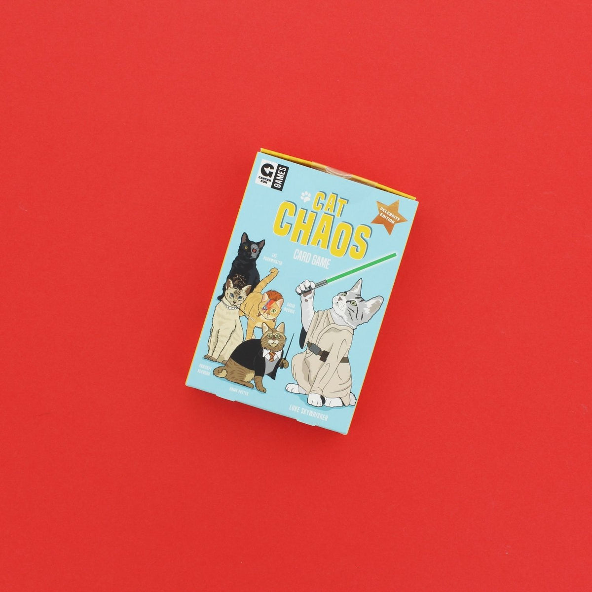 The image features the packaging of the card game &quot;Cat Chaos.&quot; It displays a vibrant blue background with illustrations of four different breeds of cats dressed in various costumes, including a Sphynx in a bat costume, a Persian in a tuxedo, a British Shorthair in a chef&#39;s outfit, and a Domestic Shorthair in a business suit.
