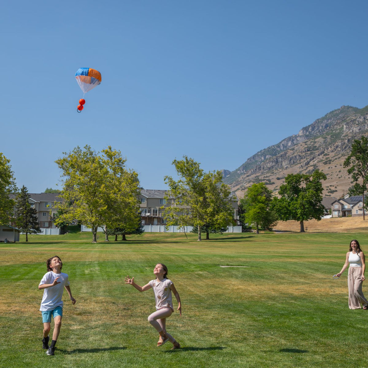 Two children chasing a ParaShoot in a park with mountains in the background