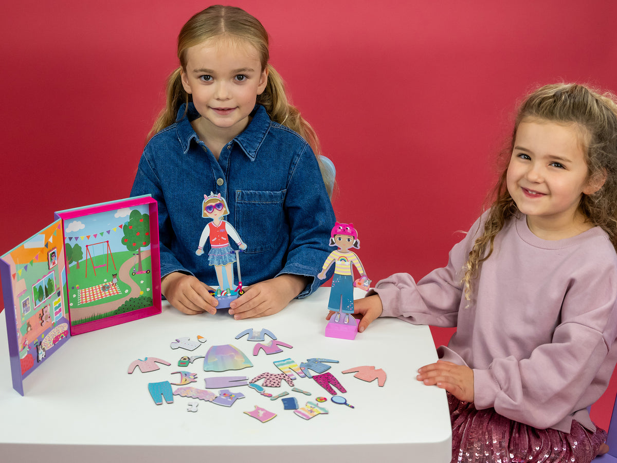 Two young girls playing with the magnetic dress up dolls at a kids table 