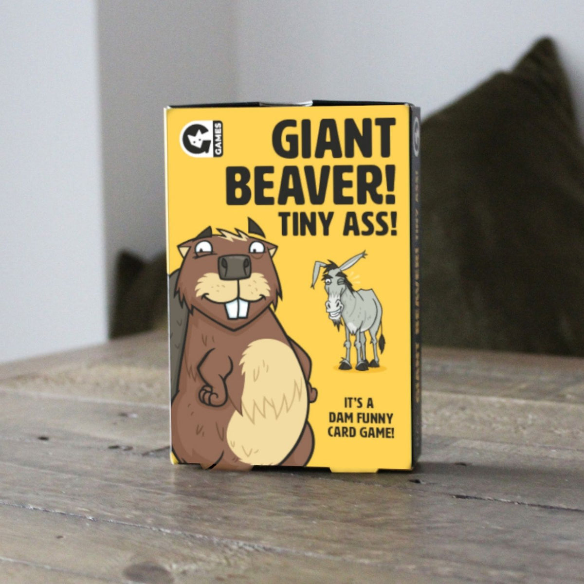 Card game box titled 'Giant Beaver! Tiny Ass!' on a wooden surface.