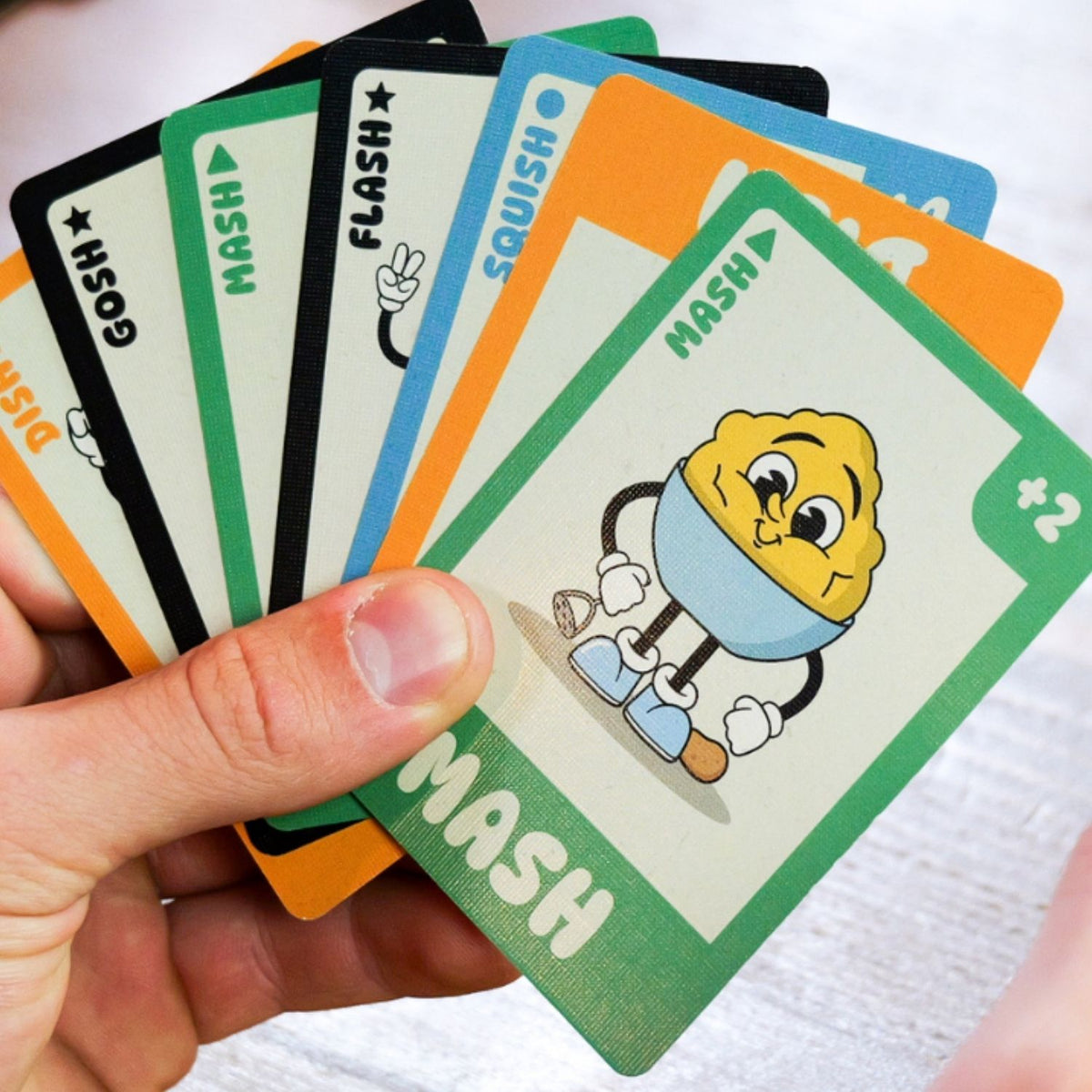 Hand holding a set of playing cards featuring cartoon character 'MASH'.