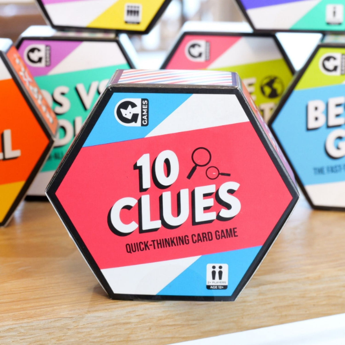 Hexagonal card game box labeled '10 Clues' on a wooden surface with other similar boxes in the background.
