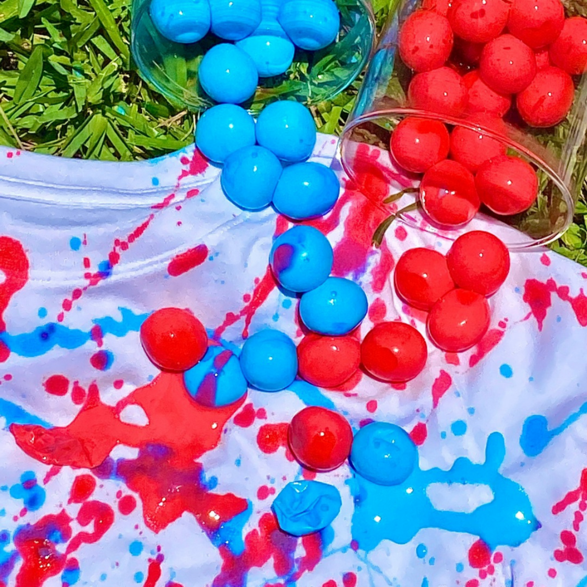 tshirt on grass with blue and red paintballs and paint splattered on it. 