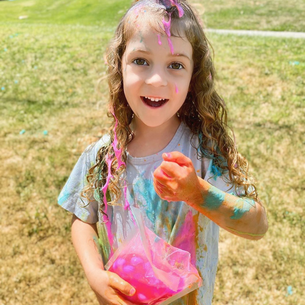 a little girl holding a packet of goblies and covered in paint