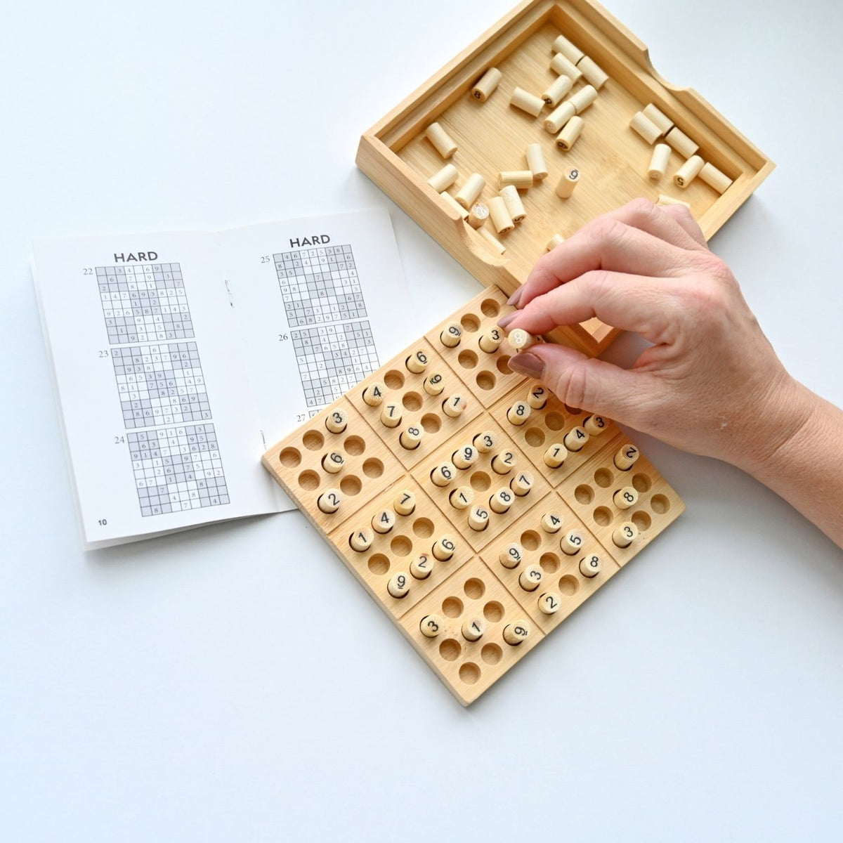 person’s hand placing a numbered bamboo tile onto the grid of the Sudoku logic game, highlighting the tactile, screen-free experience.