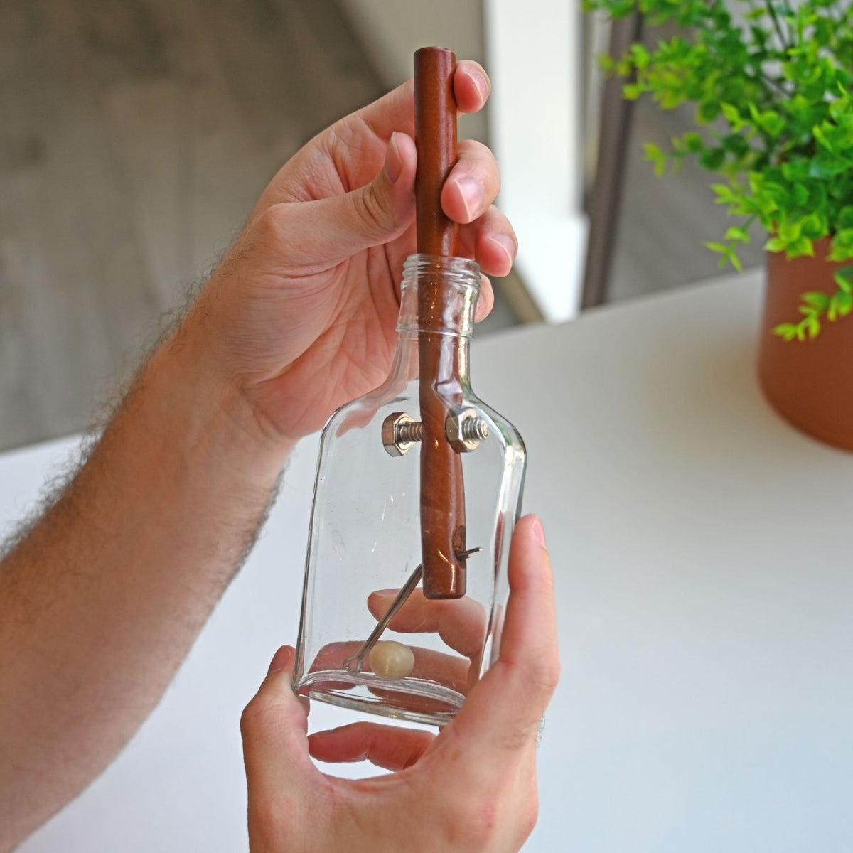 A person tilting and rotating the glass bottle puzzle to navigate the internal pieces through the neck using gravity and friction.